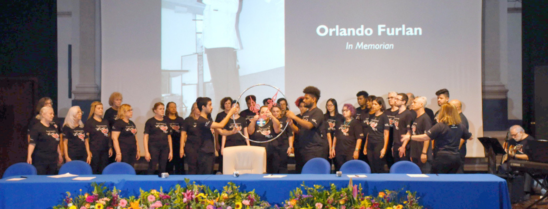 Integrantes do Coral Zíper na Boca se apresentam na IX edição do SimTec, em uma performance musical com percussão e interação com o público no palco do evento.Integrantes do Coral Zíper na Boca se apresentam na IX edição do SimTec, em uma performance musical com percussão e interação com o público no palco do evento.